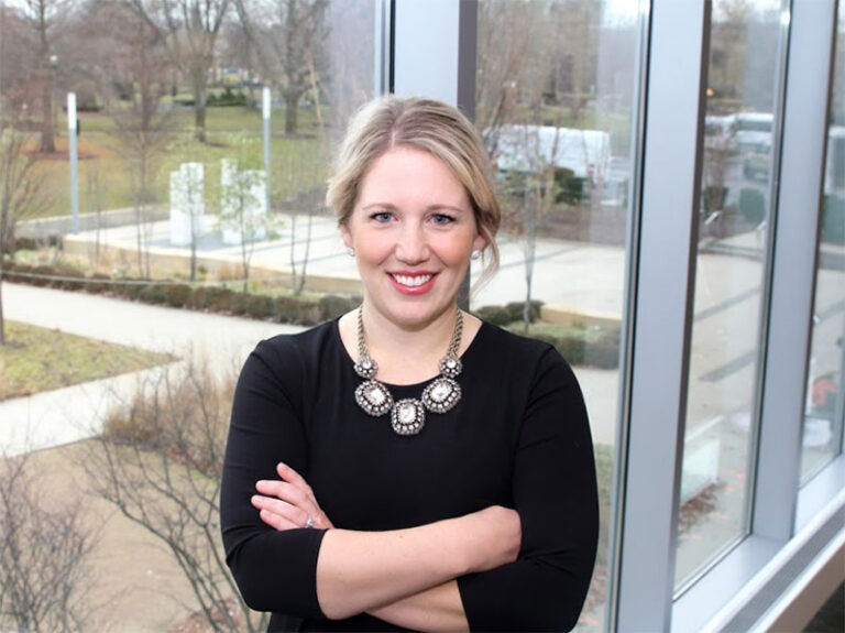 Sarah Crabtree Perez of The Overcomer Foundation standing in front of windows with her arms crossed while she smiles